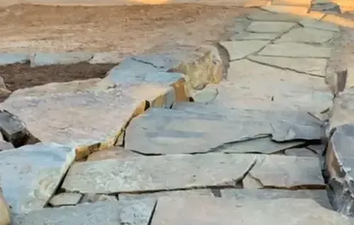 Broken stone walkway with cracked slabs and uneven gaps on a tan ground