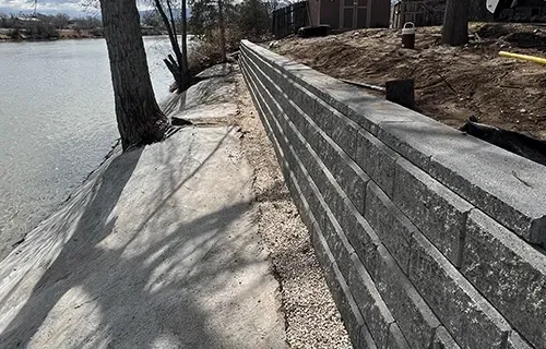 Stone retaining wall along a lakeside path with trees and a rocky shore