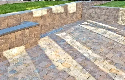 Stone steps and paved patio with sunlit shadows beside a low tan retaining wall.