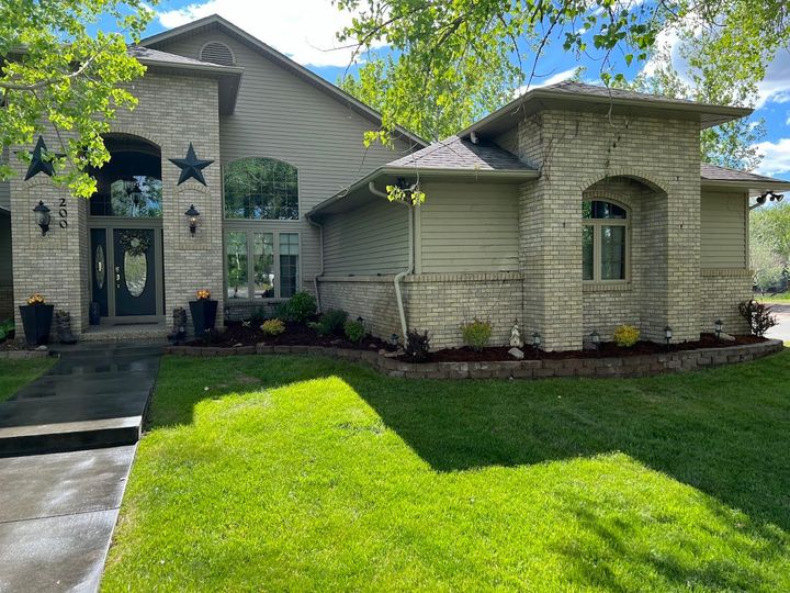 Suburban house with stone exterior, green lawn, and tree shadows in front yard