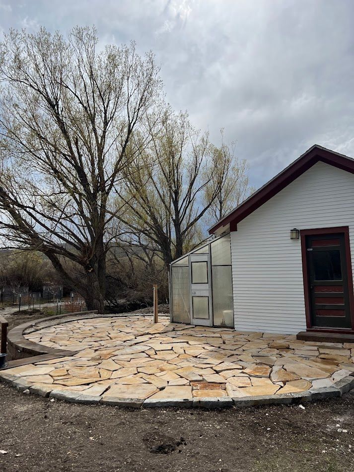 Stone-paved patio beside a white building and leafless trees under a cloudy sky.