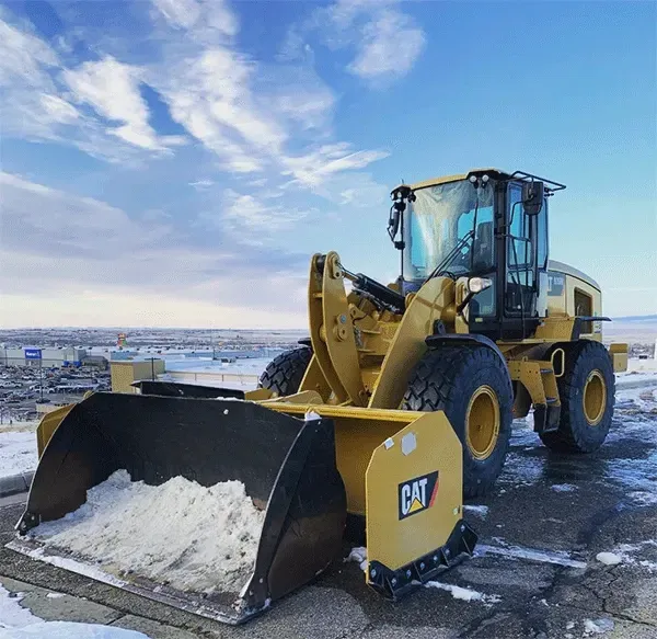 Yellow CAT wheel loader with a snow-filled bucket on a snowy road under a cloudy sky