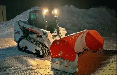 Snowplow with bright lights clearing snow at night