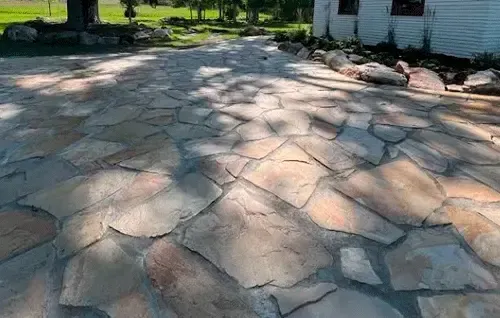 Stone-paved walkway in a park with trees and sunlight casting shadows across the path
