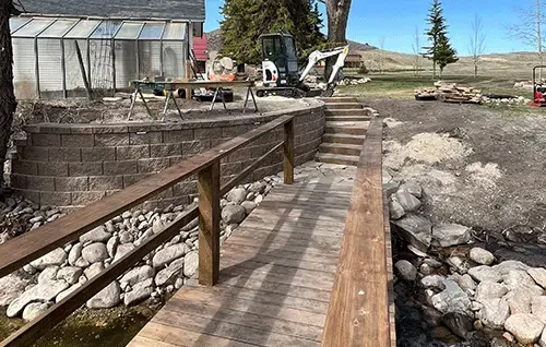 Wooden walkway beside a rocky shore, leading to a greenhouse and outdoor seating area