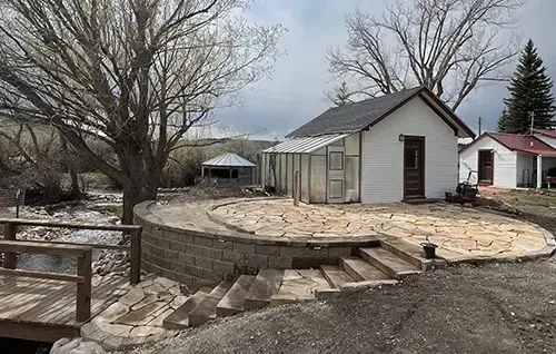 Small yard with a white shed, stone patio, and leafless trees under a cloudy sky.