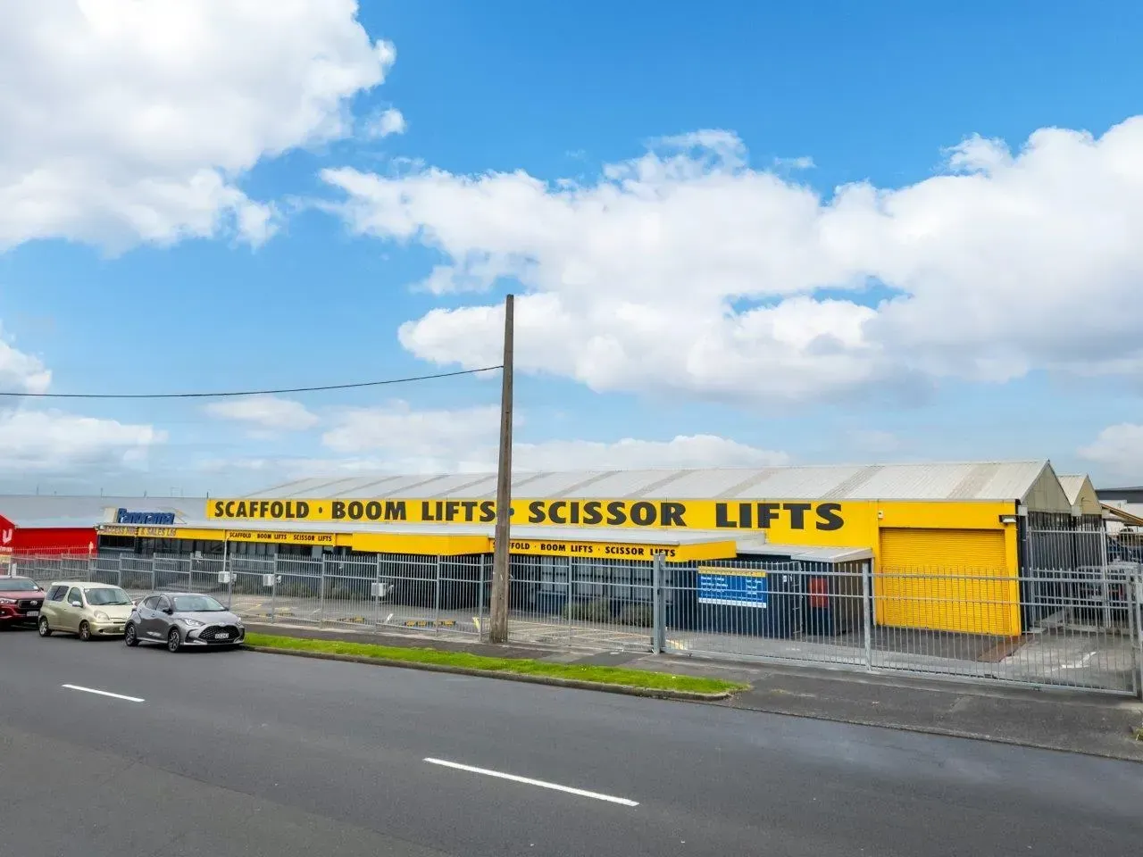 Yellow storefront for scaffold and boom lifts beside a road under a cloudy sky