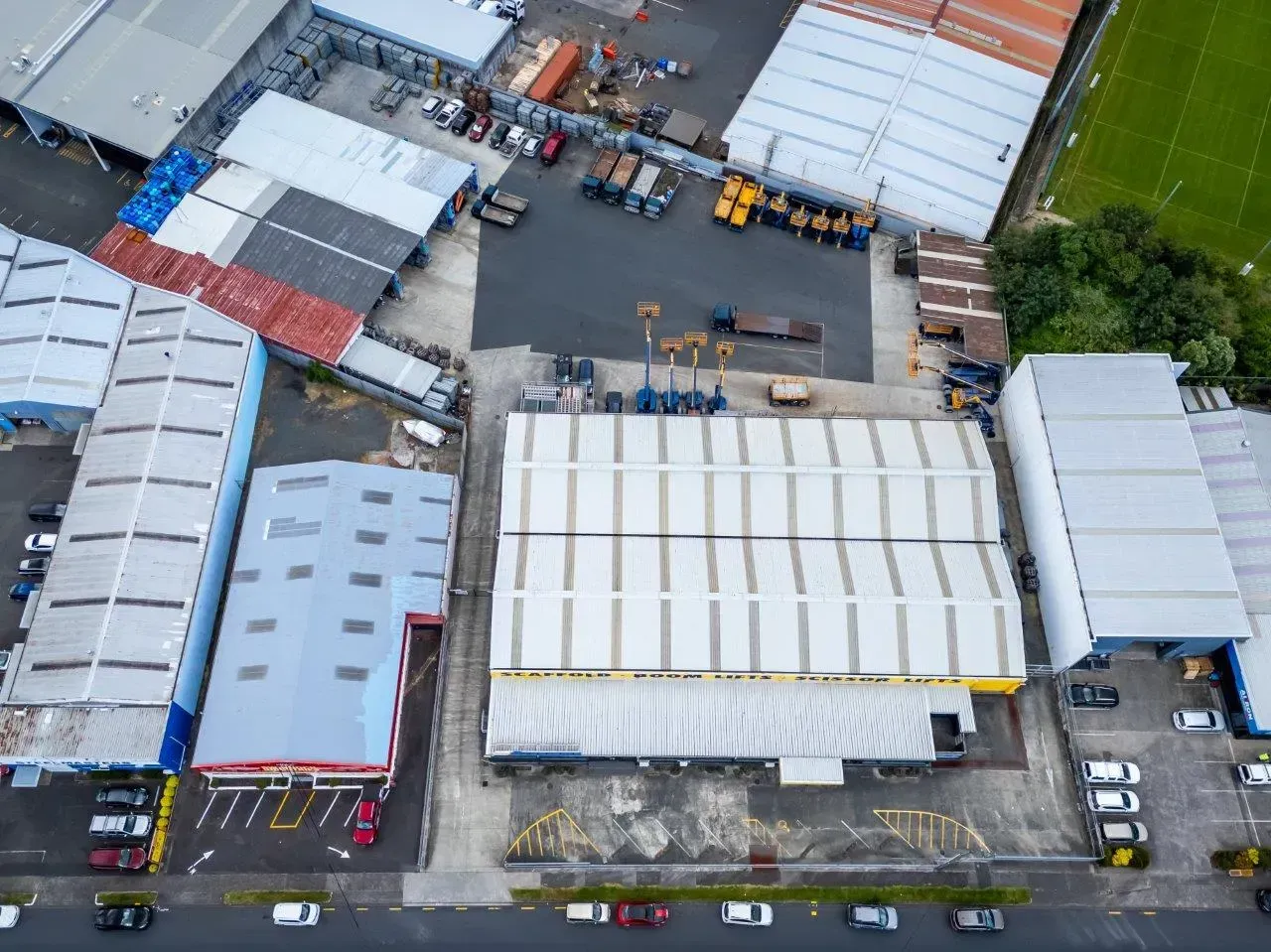 Aerial view of an industrial yard with large white-roofed buildings, parked trucks, and storage containers.