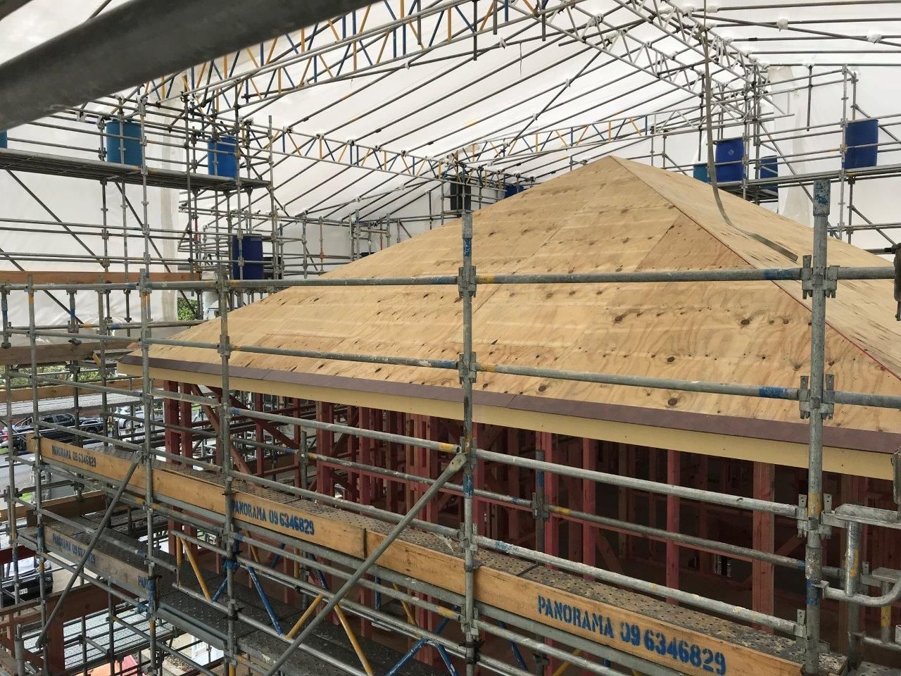 Scaffolding around a building under construction with a large roof structure covered by tan sheeting