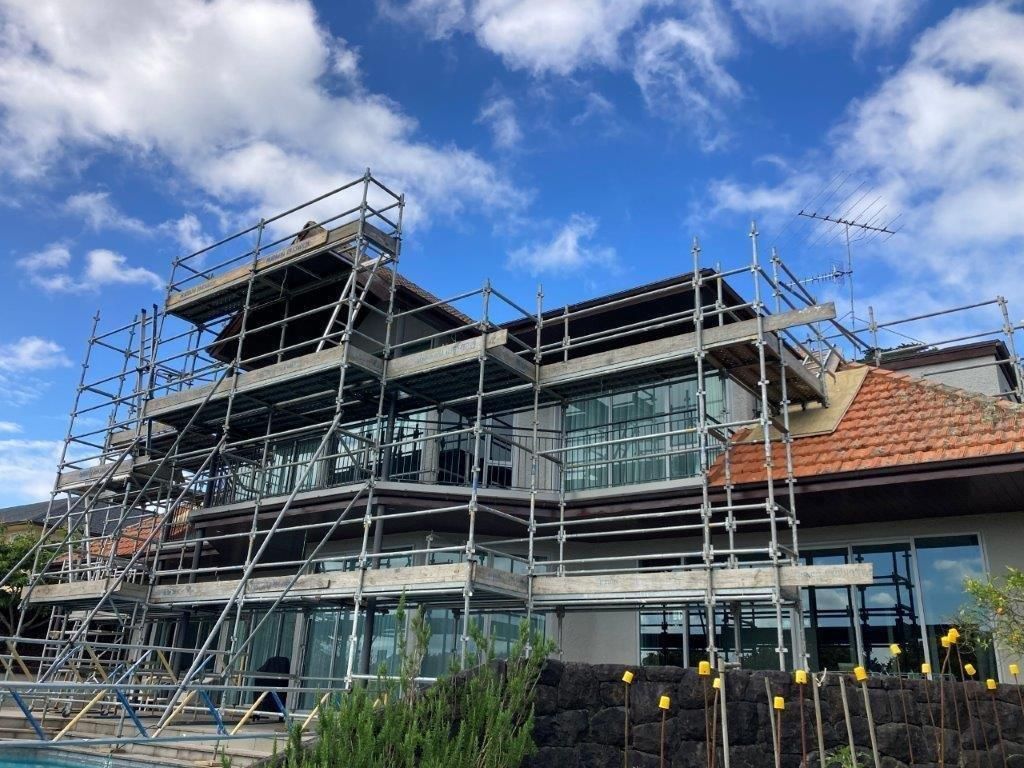 Scaffolding around a modern house with large glass windows under a blue sky