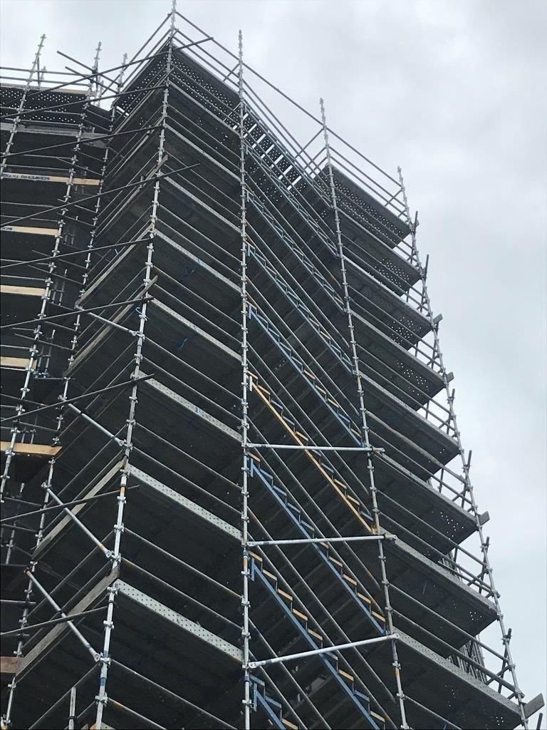 Scaffolding surrounds a tall building under construction against a cloudy sky