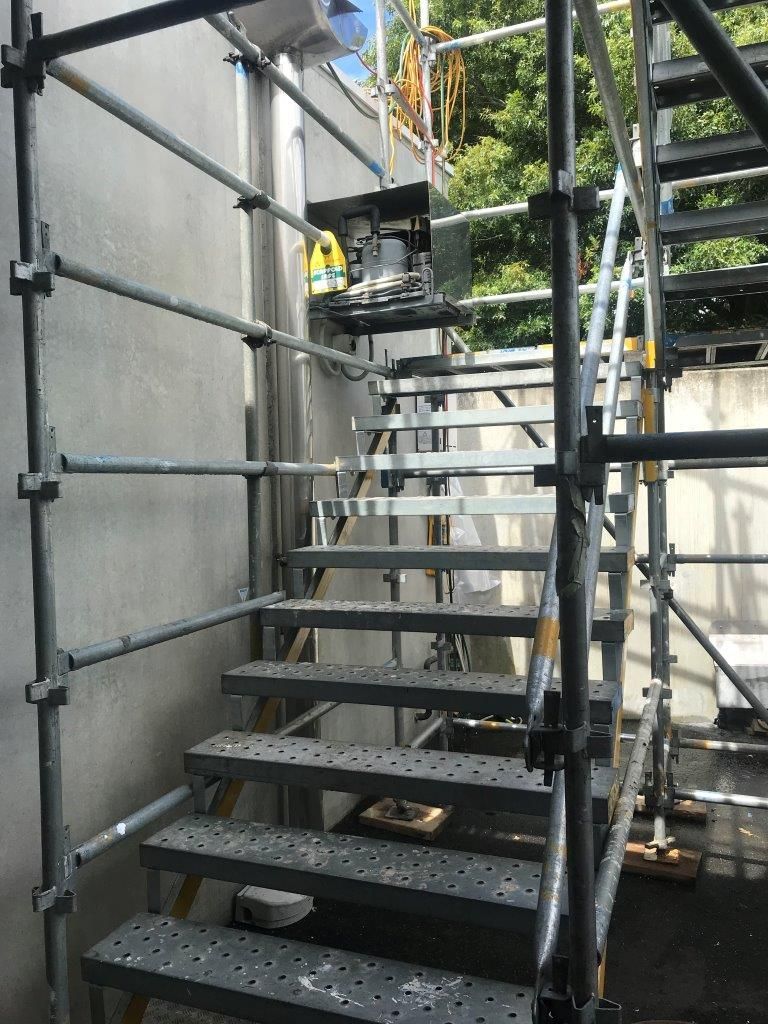 Metal stairway and scaffolding beside a building, with a worker in a yellow vest at the top.