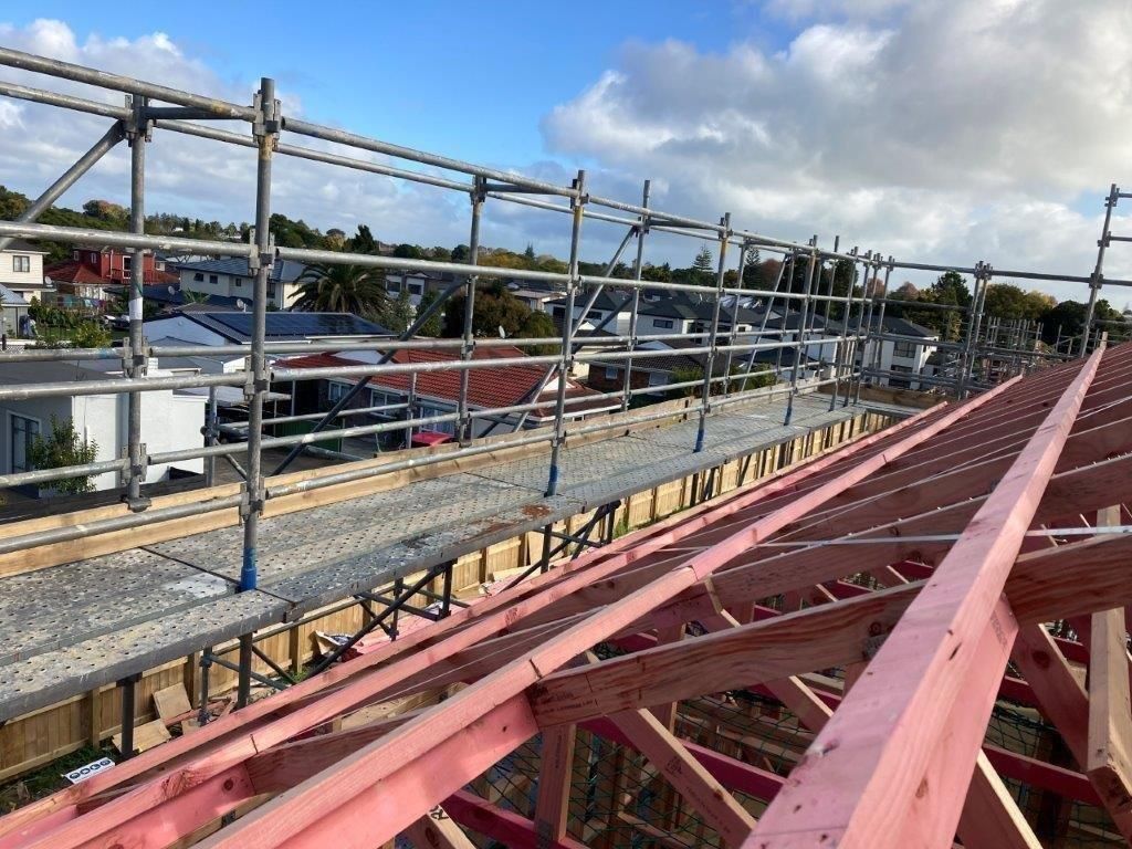Red steel roof trusses overlooking a construction site with scaffolding and a cloudy sky