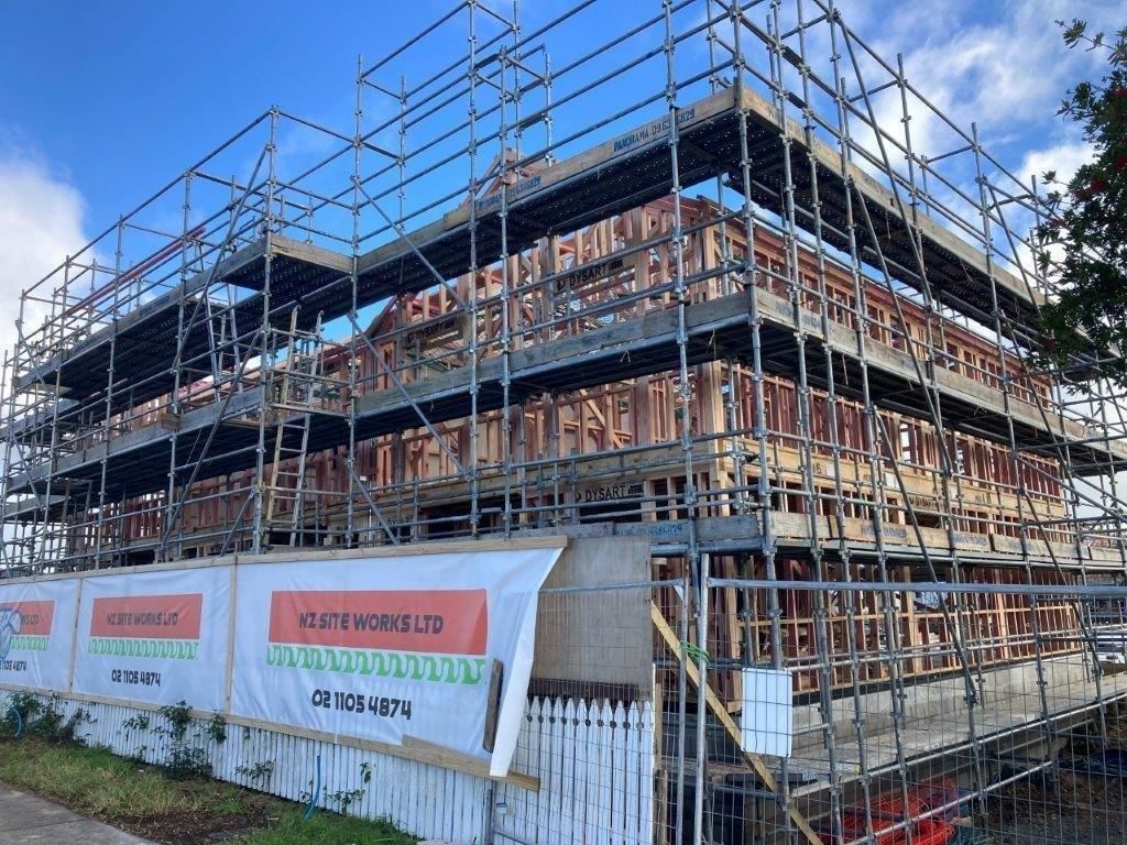 Scaffolding around a multi-story building under construction behind a fence and signs