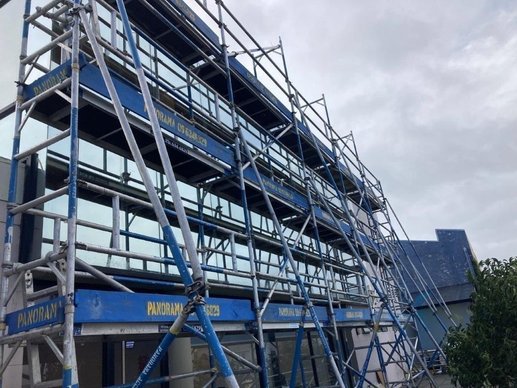 Scaffolding around a building under construction with blue safety netting and a cloudy sky