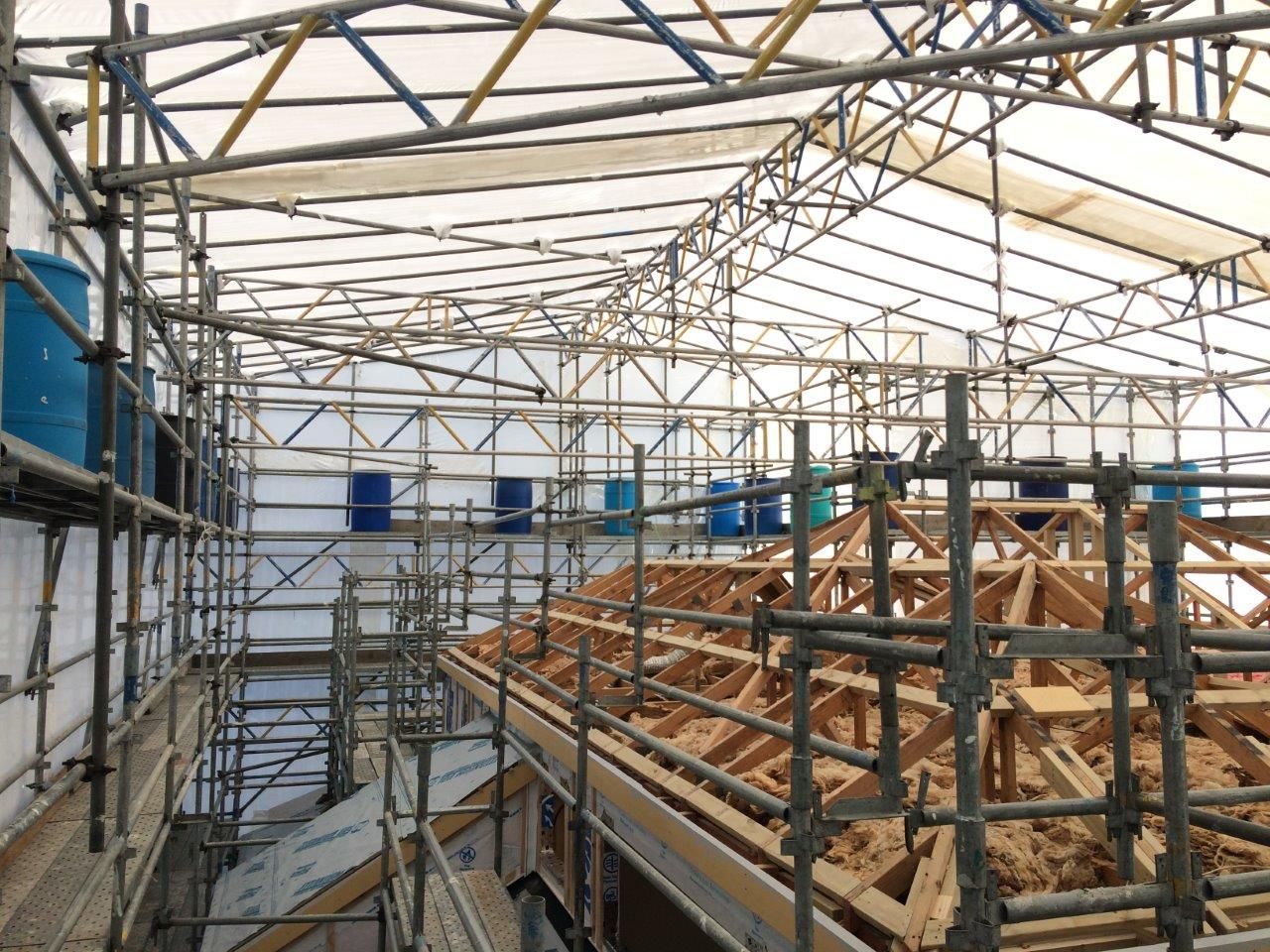 Interior of a scaffolding-covered roof under construction, with exposed wooden trusses and metal framing.