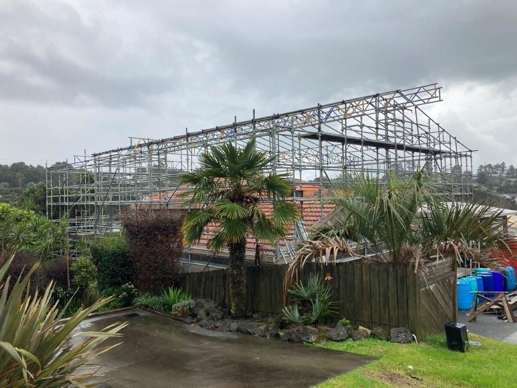 Partially built house frame behind a garden fence on a cloudy day