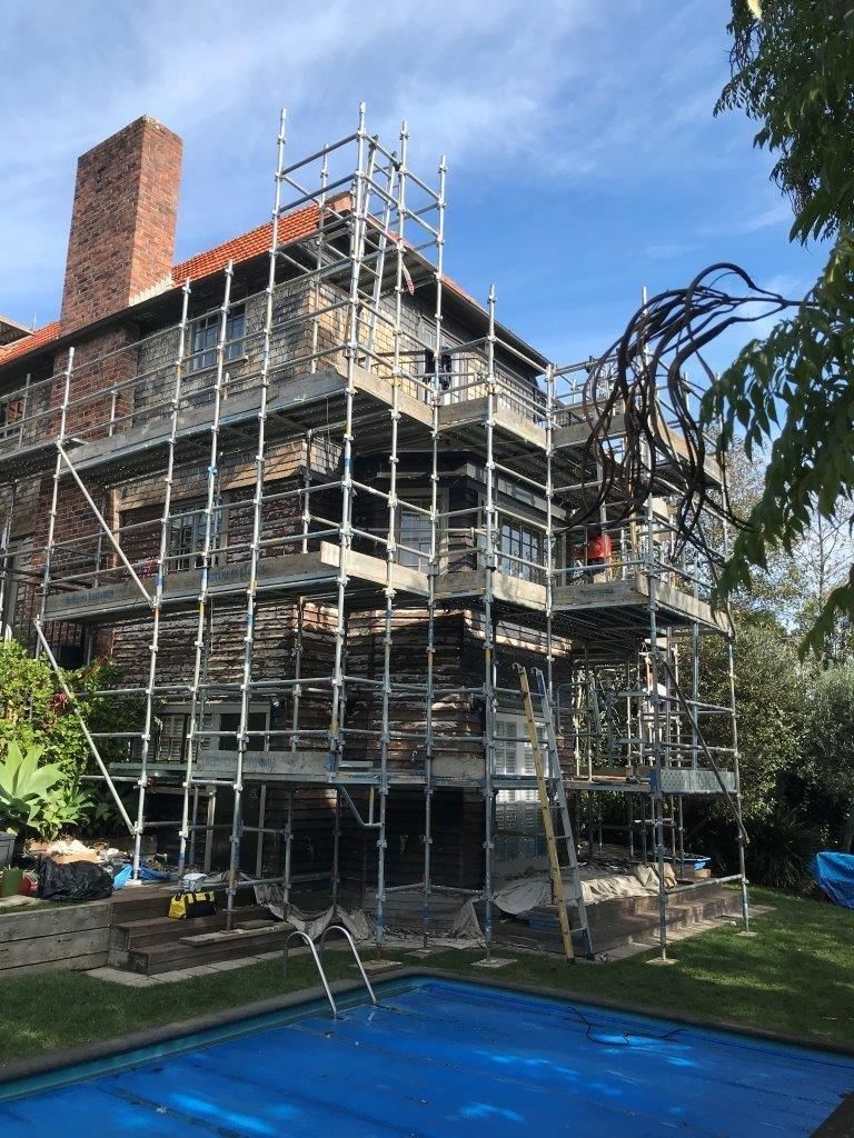 House under renovation with full scaffolding beside a backyard pool