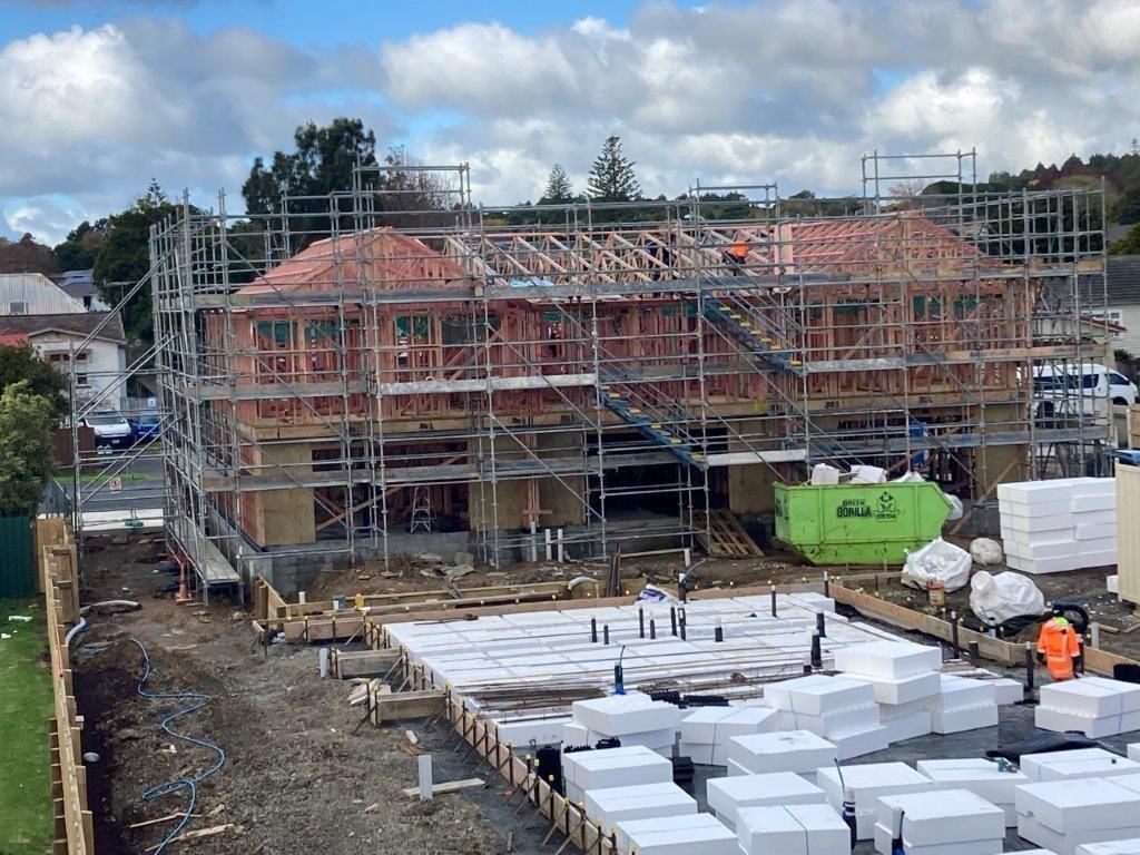 Construction site with scaffolded houses, red tiled roofs, and stacks of white building blocks in the foreground