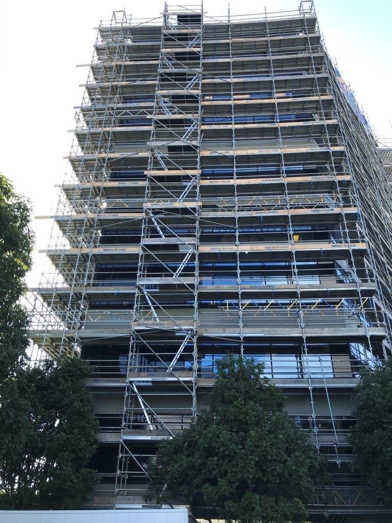 Tall building wrapped in scaffolding, seen from below against a bright sky