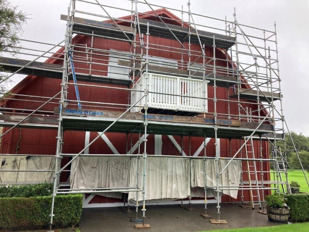 Red house under renovation with scaffolding and covered lower windows and entrance