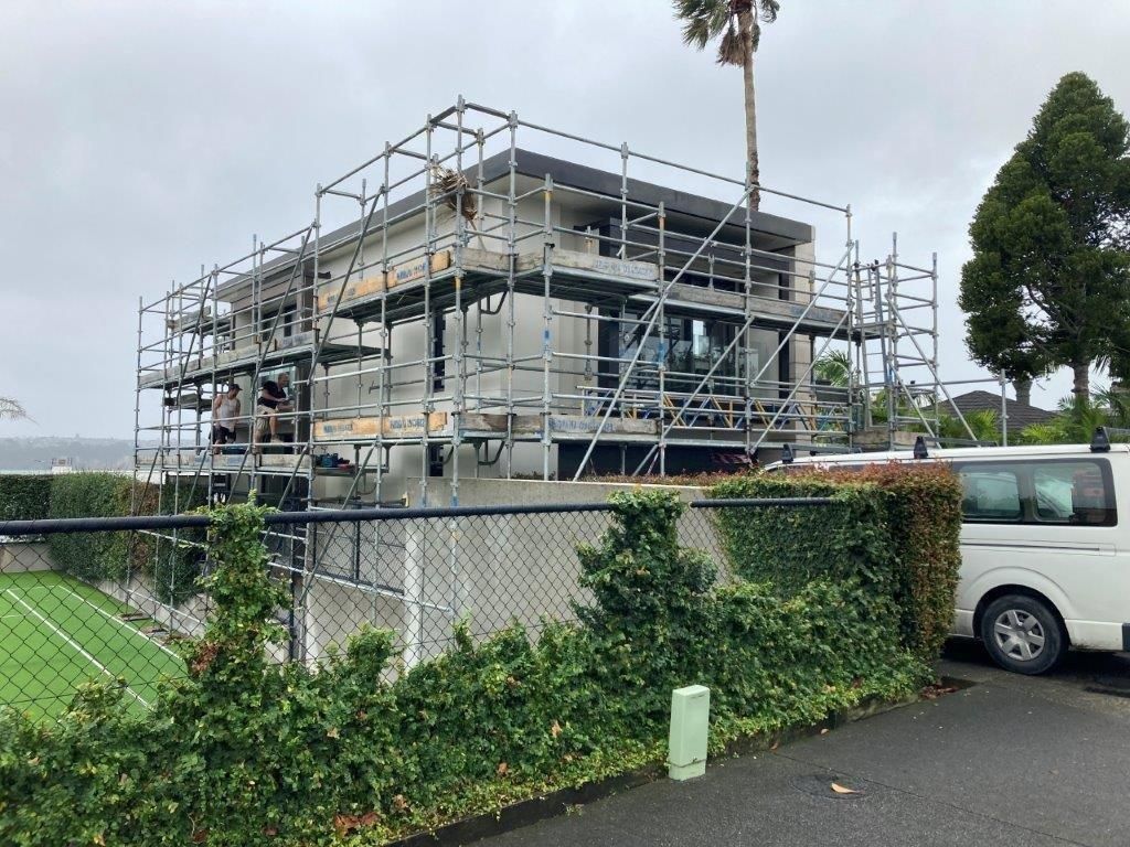 Modern house under construction with scaffolding beside a parked white van and greenery