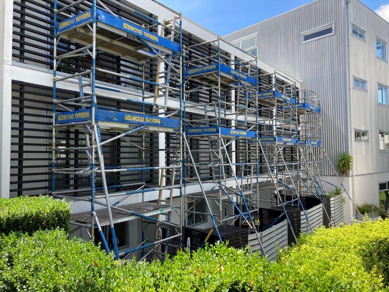 Scaffolding beside a building under construction, with blue and silver metal frames in front of a gray facade.
