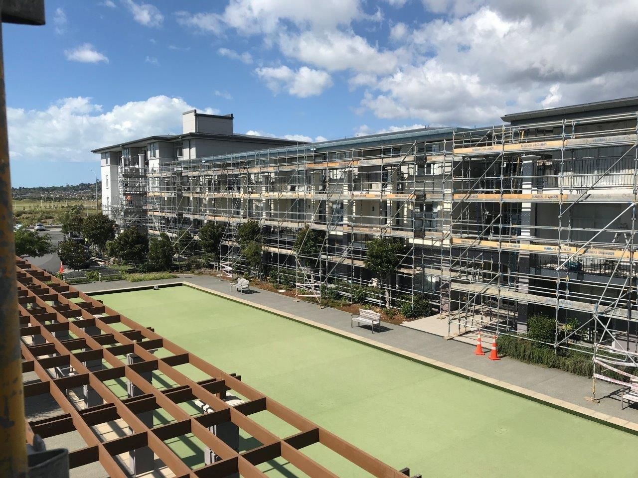 Scaffolded building beside a green courtyard under a partly cloudy sky