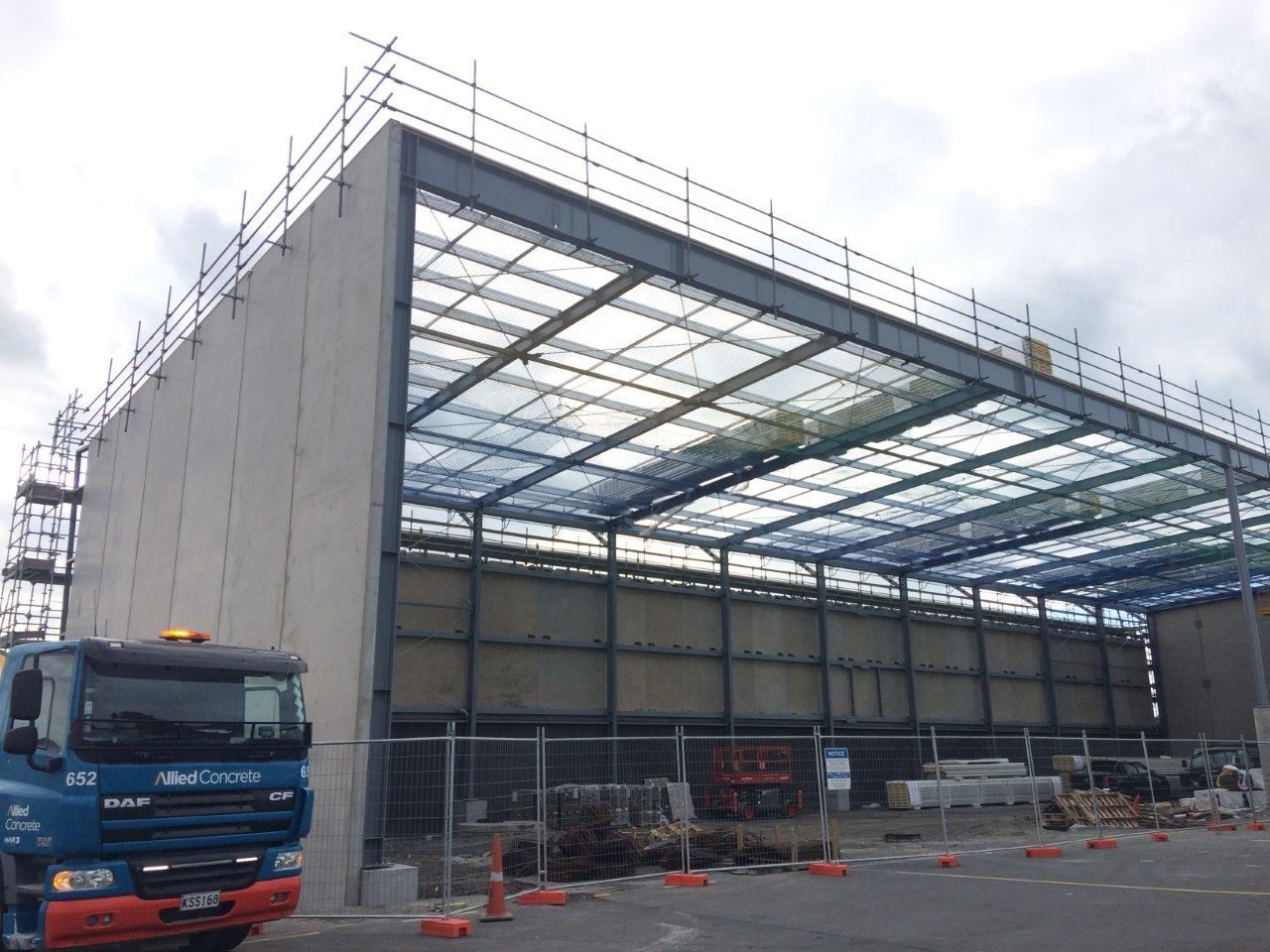 Large warehouse under construction with steel frame, blue truck, and scaffolding outdoors