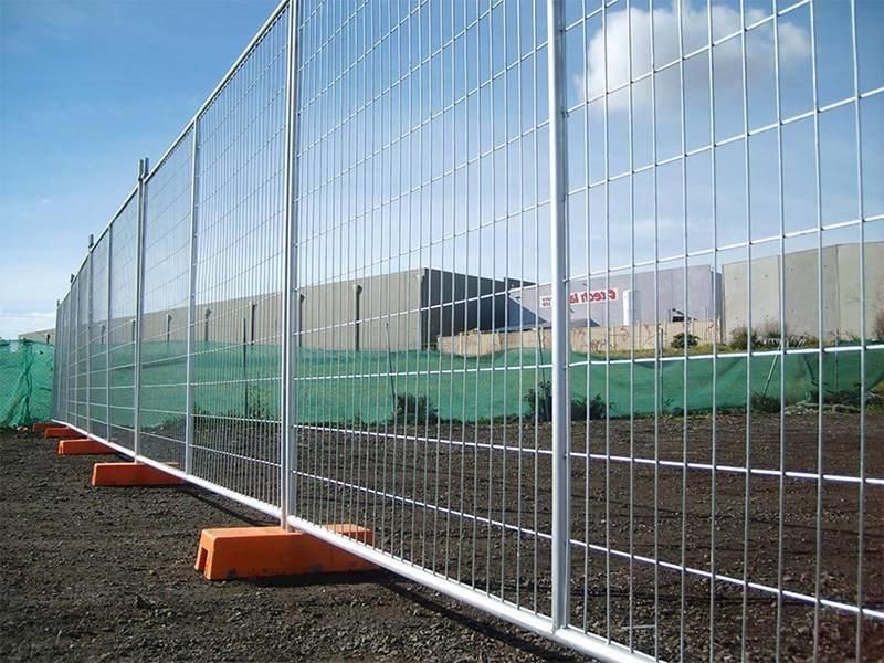 Temporary white wire fence beside a construction site, secured with orange bases and green mesh behind it