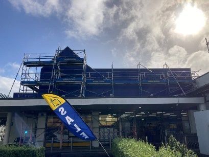 Scaffolding on a building under construction, with a blue-and-yellow flag in front and cloudy sky above