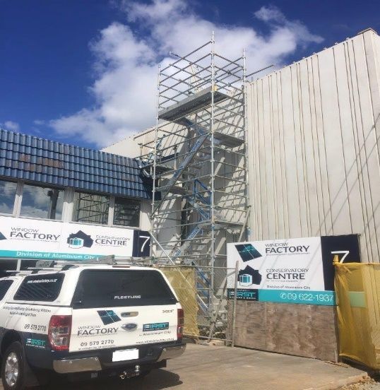 Construction site with scaffolding beside a factory center building and a white utility truck in front
