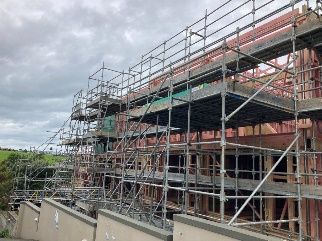 Scaffolding around a red brick building under construction beside a road, under cloudy skies