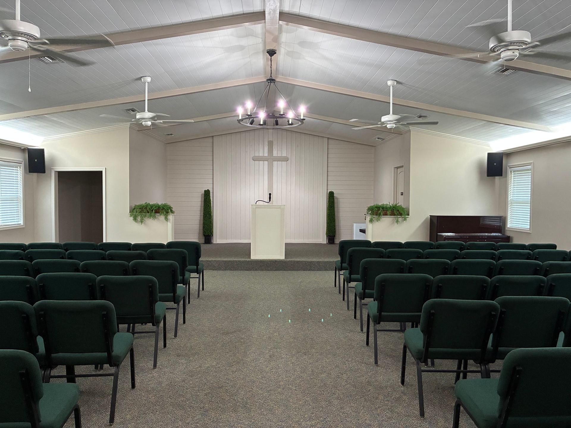 Empty chapel with rows of green chairs facing a lectern and cross on the front wall.