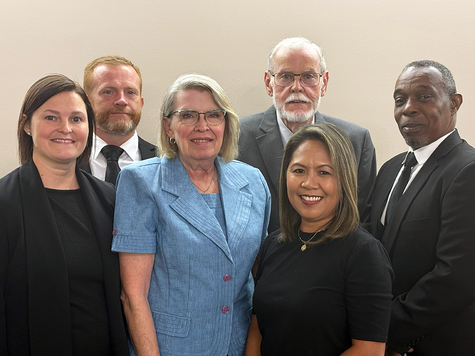 Six people posing for a group portrait indoors, wearing business attire.