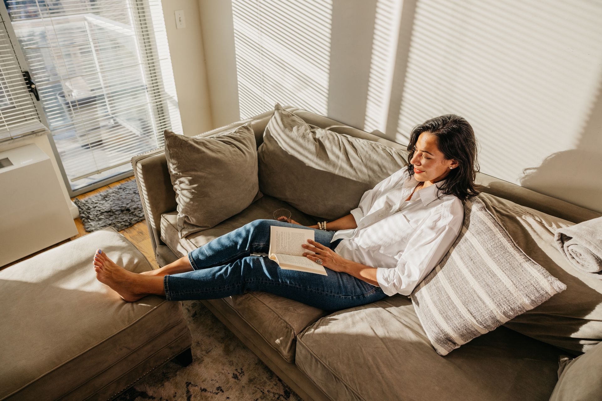 A woman is sitting on a couch reading a book.