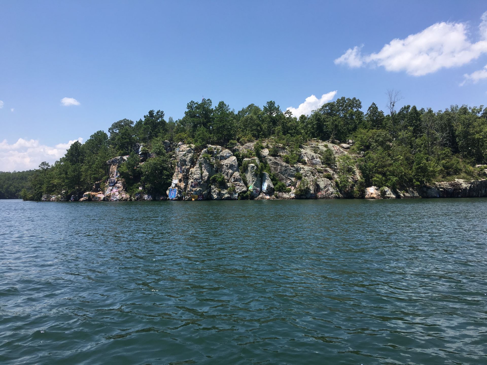 Rocky, tree-covered shoreline beside blue water under a clear sky