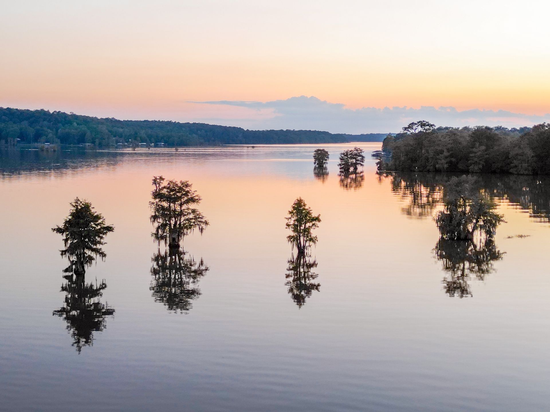 Flooded lake at sunset with trees rising from calm water and distant shoreline silhouettes