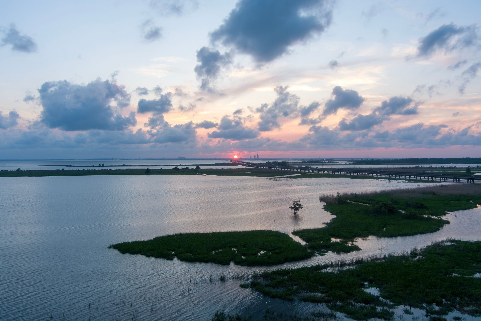 Sunset over a calm lake with marshy islands and cloudy pink-blue sky