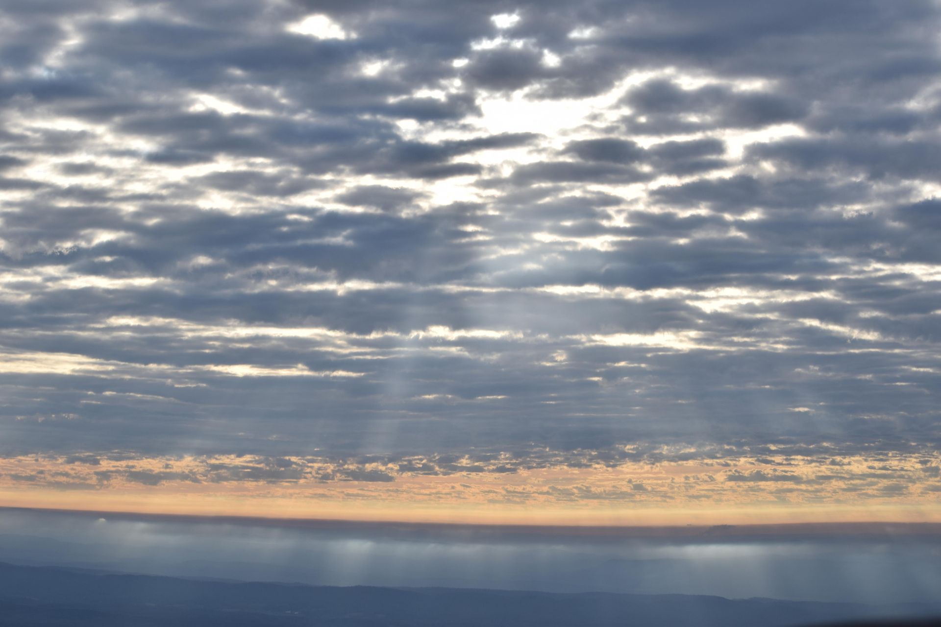 Cloudy sunset over calm water, with sunbeams breaking through the clouds.
