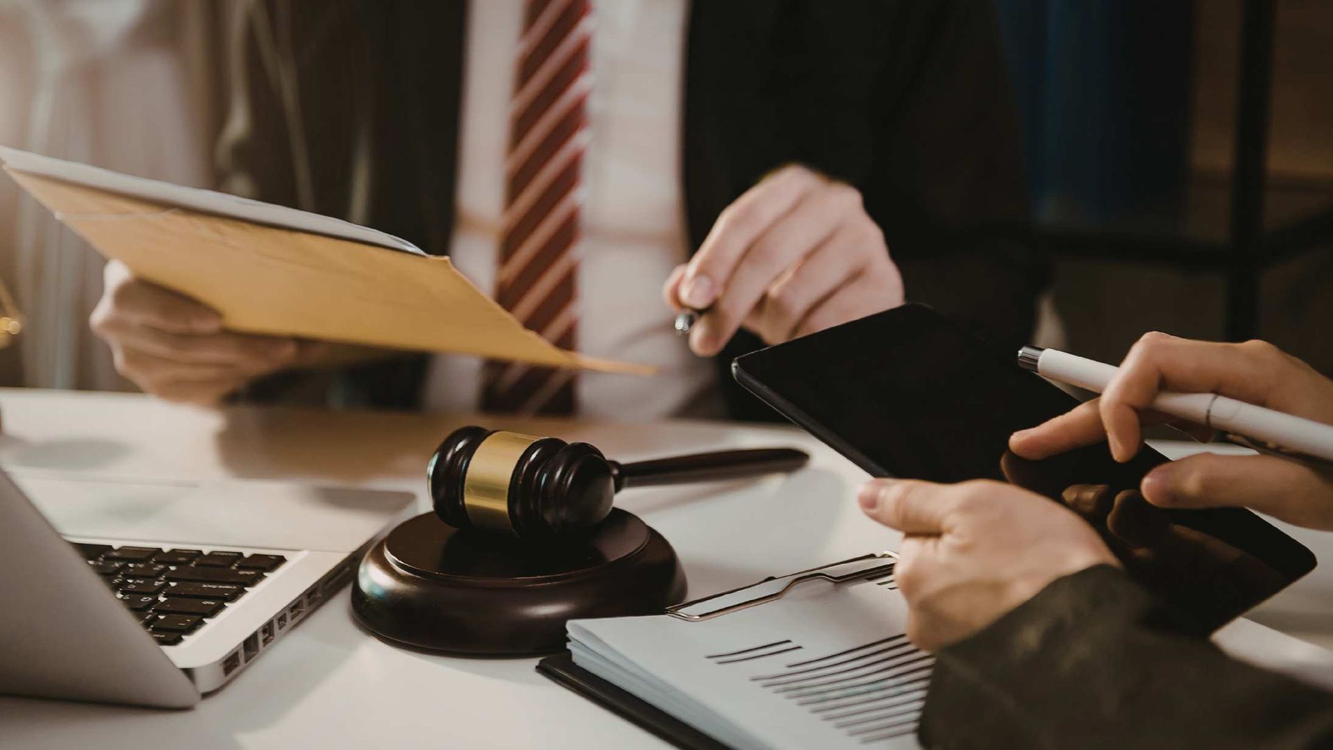 Meeting table with laptop, documents, gavel, and hands reviewing a contract.