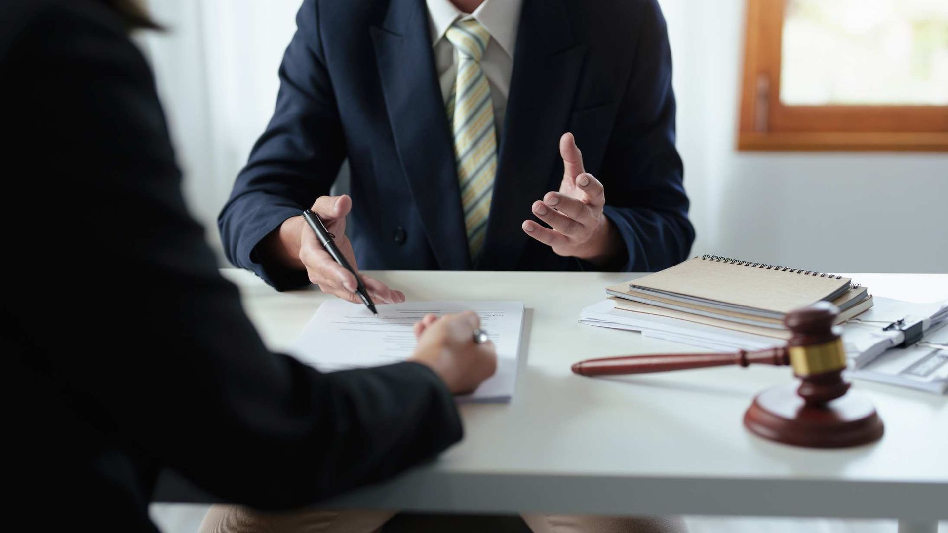 Business meeting with two people signing documents at a desk, with a gavel and notebook visible.