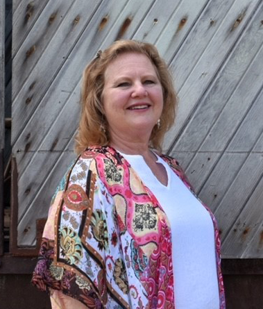 Smiling woman in a pink patterned shawl standing outdoors before a wooden wall