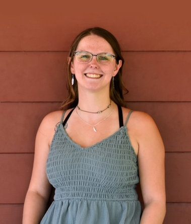 Smiling woman in glasses and a blue dress standing against a red wall