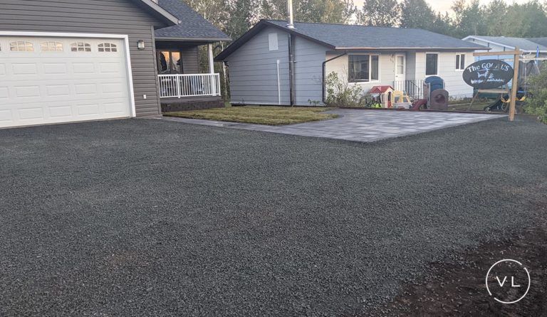 Gravel driveway and paved patio area leading to a house and garage; gray, blue, and green tones.