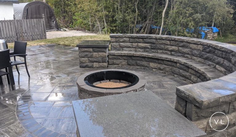 Stone fire pit with curved stone seating on a wet, gray stone patio.