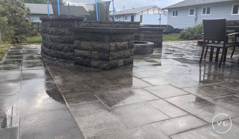 Wet stone patio with built-in seating area and fire pit in a backyard setting.