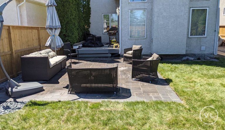 Patio with outdoor furniture, including sofa, chairs, and umbrella, set on a stone patio with a green lawn.