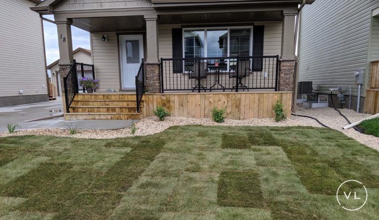 A beige house with a wooden porch and newly laid sod in the front yard.