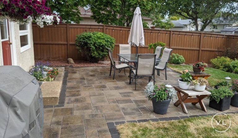 Patio with table, chairs, umbrella, and potted plants in a backyard setting with a brown fence.
